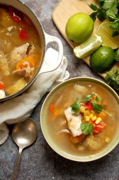 two bowls of soup on a table with limes, cilantro and other ingredients