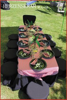 a table set up with black and red striped cloths, plates and potted plants