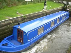 a large blue boat floating down a river next to a lush green field with people standing on it