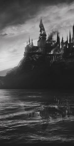 black and white photograph of hogwarts castle from across the water at sunset with dark clouds