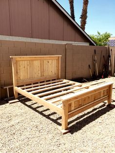 a wooden bed frame sitting in the middle of a yard next to a fence and palm trees