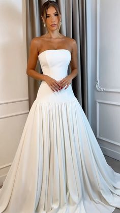 a woman in a white wedding dress standing next to a window with her hands on her hips