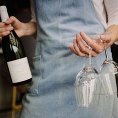 a person holding two wine glasses in their hands and one is holding a bottle with the other hand