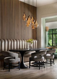 a dining room table with chairs and lights hanging from the ceiling above it, along with an upholstered wall