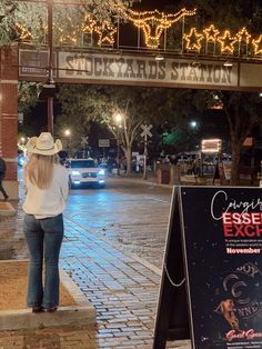 a woman standing in front of a sign on the side of a road at night