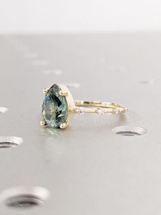 a close up of a ring with a green stone in it on a silver surface