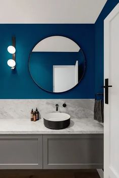 a modern bathroom with blue walls and marble counter tops, round mirror above the sink