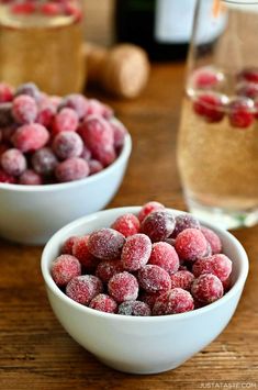 two white bowls filled with frozen berries on top of a wooden table next to a glass of wine