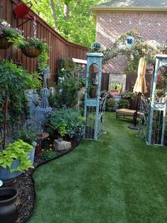 an outdoor garden with lots of plants and potted plants on the grass in front of a brick building