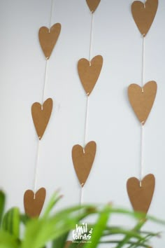 some brown hearts hanging from a string on a white wall next to a potted plant