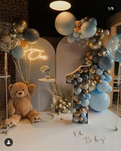 a teddy bear is sitting in front of balloons and letters on the floor at a baby's first birthday party