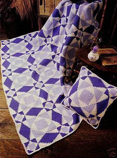 a purple and white quilt sitting on top of a wooden floor next to two pillows