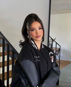 a woman standing in front of a staircase wearing a black jacket with white stripes on it