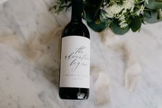 a bottle of wine sitting on top of a marble table next to flowers and ribbon