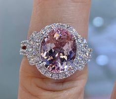 a close up of a person's hand holding a pink and white diamond ring