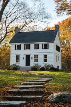 a white house with steps leading up to the front door and windows in fall foliage