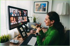 a woman sitting at a desk in front of a computer screen with people on it