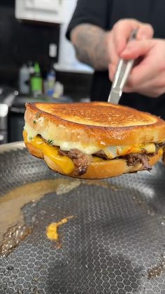 a man is cutting into a sandwich on a pan with a knife and tongs