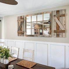 a dining room table with two mirrors hanging on the wall and flowers in vases