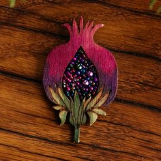 a brooch with flowers on it sitting on top of a wooden table next to plants