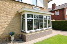 a brick house with white windows and a potted plant in the front garden area