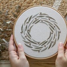 two hands are holding up a white embroidery hoop with brown leaves on it, while another hand is holding the hoop