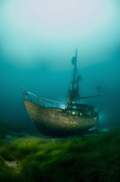 an old wooden boat in the ocean with grass on the bottom and water around it