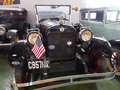 an old model car is on display in a museum with other antique cars behind it