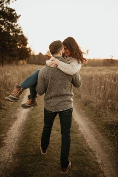 a man carrying a woman on his back while walking down a dirt road in the middle of a field