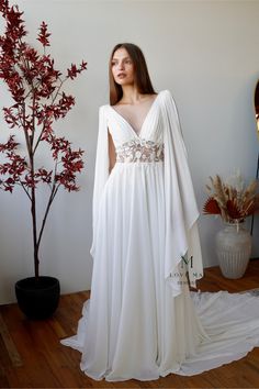 a woman in a white wedding dress standing next to a tree with red leaves on it