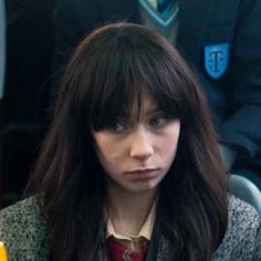 a woman with long hair sitting at a table in front of two other people and one is looking off to the side