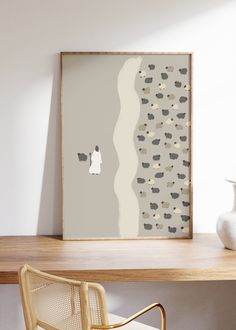 a white vase sitting on top of a wooden table next to a framed wall art