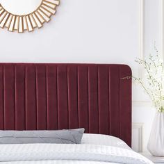 a bed with a red velvet headboard next to a white vase and mirror on the wall