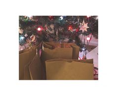 several brown paper bags with christmas decorations on the top and bottom, all lined up in front of a christmas tree