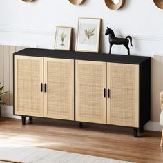 a sideboard with wicker doors and black handles in a room decorated with framed pictures