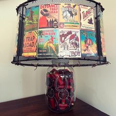 a lamp shade made out of magazines on top of a wooden table next to a jar filled with red apples