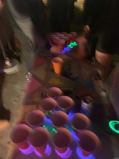 several people standing around a table with cups on it and neon lights in the background