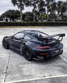 a black porsche sports car parked in a parking lot with palm trees behind it,