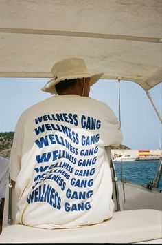 a man sitting on the back of a boat wearing a t - shirt that says wellness gang