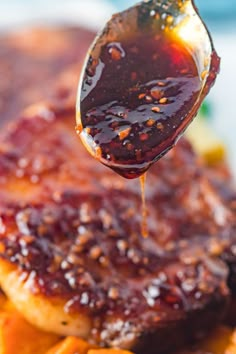 a close up of a spoon with food on it and sauce being drizzled over the meat