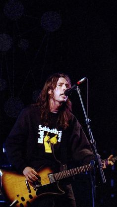 a man with long hair playing guitar in front of a microphone and microphone on stage