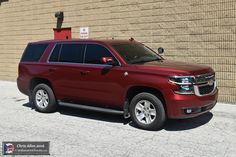 a red chevrolet suburban parked in front of a brick wall with no parking sign on it