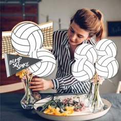 a woman sitting at a table with flowers and vases in front of her holding up some paper art work