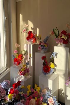 several vases filled with flowers sitting on top of white cubes in front of a window