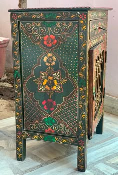 an ornately painted cabinet sits on the floor in front of a potted plant