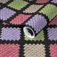 a multicolored crocheted pattern on a black background with a roll of tape