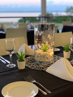 the table is set with white plates, silverware and glass vases filled with plants