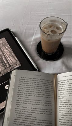 an open book sitting on top of a table next to a cup of coffee and tablet