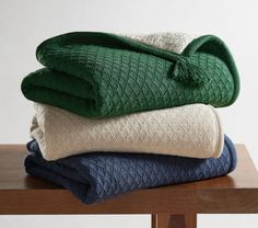 three folded blankets stacked on top of each other in different colors and patterns, sitting on a wooden table