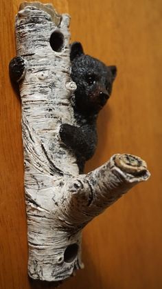 a small black bear sitting on top of a tree branch next to a wooden wall